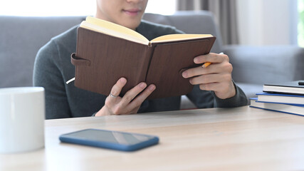 Cropped shot of young man reading book and relaxing in living room.