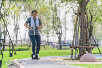 asian woman ridding on kick scooter on pavement in park