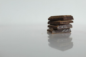 Dark bitter chocolate pieces stacked slide lies on a white background with a reflection with a...
