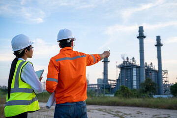 Two engineers working with laptop at front oil and gas refinery plant industry factory.