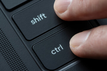 Fingers holding down Shift and Ctrl keys together on a black laptop computer.