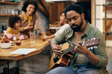 African American father playing acoustic guitar at home.