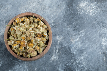Wooden bowl of dried chamomile on marble background