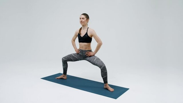 The young girl performs wide squats, does Pilates. The girl practices yoga on a gymnastic mat. The girl is engaged in sports, fitness. Active lifestyle. Isolated on a white background