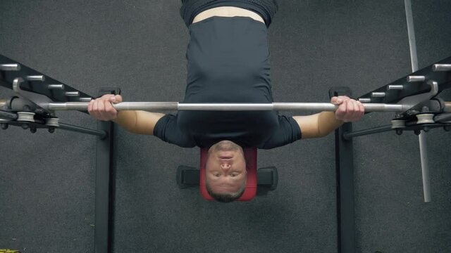 Gym workout. Powerlifter bulk up chest muscles. Bodybuilder at the gym lifts an iron barbell on the Smith Machine. Handheld shot, view from the top.