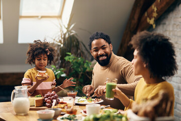 Happy black family talking while having breakfast at home.