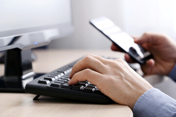 Man using smartphone on PC keyboard background. Concept of online communication, office or home work and payment