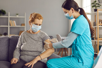 Mature woman gets vaccinated at home. Professional nurse or doctor disinfects skin on senior...