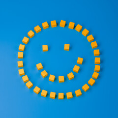 Fototapeta premium Smiley symbol composed of wooden yellow cubes on blue background. Top view, closeup
