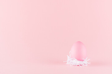 Cute easter egg standing in white nest on pastel pink background, copy space.