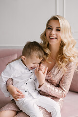 Beautiful young mother and son cuddle and play in smart clothes at home