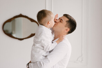 Beautiful young dad and son cuddle and play in smart clothes at home