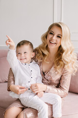 Beautiful young mother and son cuddle and play in smart clothes at home