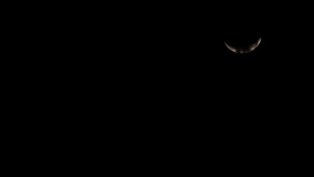 Waxing Crescent Moon, 4K Time Lapse, going down from the top right corner of the frame as seen through the clouds and then disappears into the dark with light orange colour.