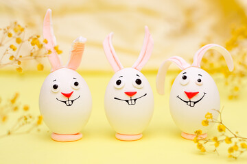 Happy Easter concept.Creative Easter bunnies made of eggs with funny faces painted on them.Yellow background,fresh flowers.