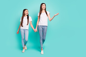 Fototapeta premium Full length body size photo of two curious sisters holding hands walking forward talking looking copyspace isolated bright blue color background