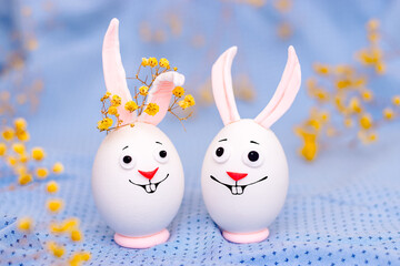 Happy Easter concept.Creative Easter bunnies made of eggs with funny faces painted on them.Blue background,fresh flowers.