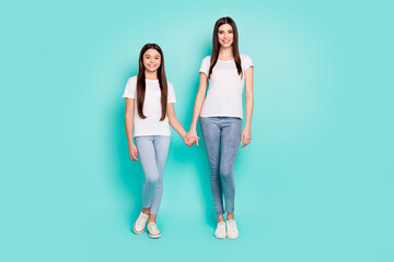 Obraz premium Full length body size photo of two cheerful sisters holding hands isolated on bright blue color background