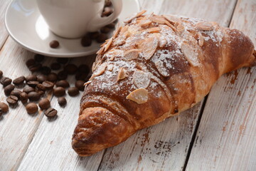 Fresh croissant with a cup of coffee, roasted beans on vintage background