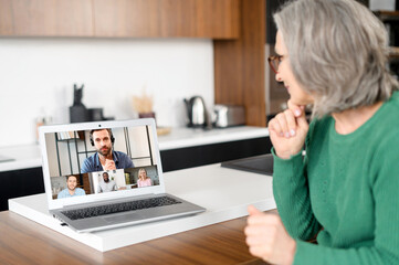 Smiling entrepreneur, aged woman sitting at the laptop, home, meeting with the business partners to...