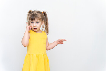 child girl in a yellow dress points to a gray background near herself. smart look, learning