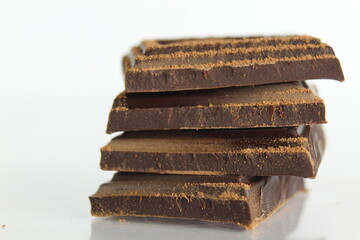 Dark bitter chocolate pieces stacked slide lies on a white background with a reflection with a place for text and copyspace