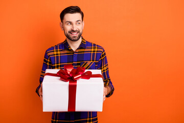 Portrait of satisfied person arms hold giftbox look interested empty space isolated on orange color background
