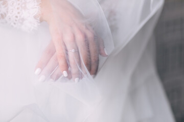 the bride's hands with white manicure holds on the dress under the veil.