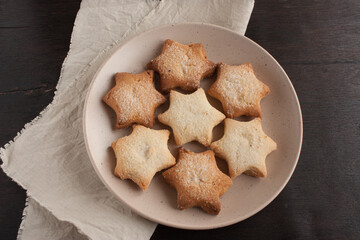 Delicious homemade cookies in the shape of stars sprinkled with sugar. Laid out on a plate on a dark wooden table with a linen napkin.