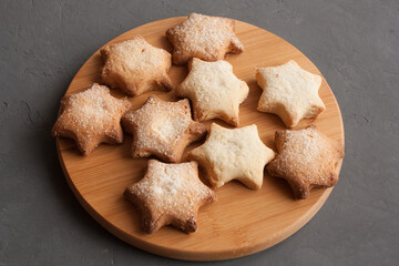 Delicious homemade cookies in the shape of stars sprinkled with sugar. Laid out on a kitchen board on a dark gray background.