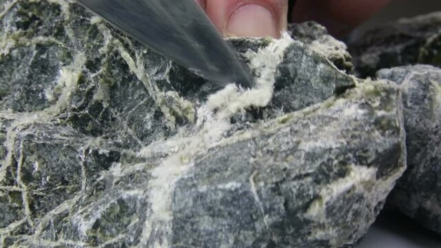 The blade of the knife picks and pulls out the asbestos fibers from the stone.