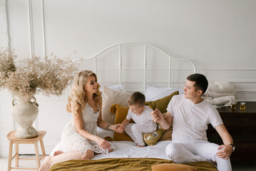 Beautiful young family man woman and son in white clothes play on the bed at home