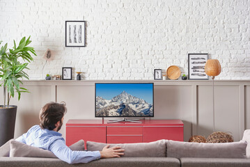 Man is watching television in the decorative room, red unit, white brick wall, frame lamp concept, close up screen style.