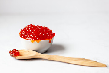 a wooden spoon with red caviar is placed next to a white cup full of red caviar