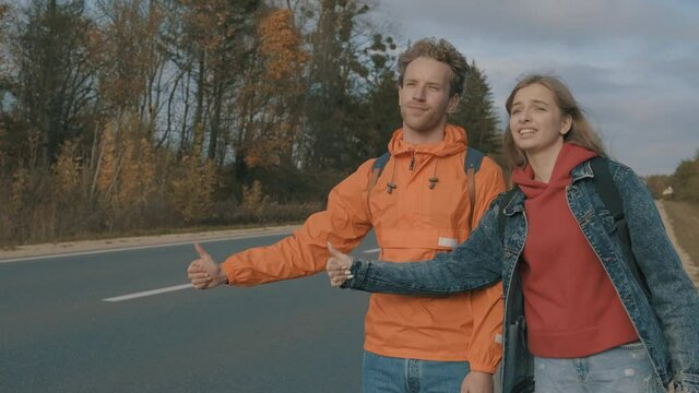 Hitchhikers. Young male and female backpackers hitchhiking. Road trip.