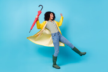 Photo of pretty funky dark skin lady wear yellow overcoat walking holding parasol looking empty space isolated blue color background © deagreez