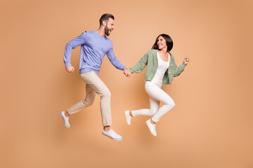Fototapeta na wymiar Full length body size view of nice cheerful life partners jumping holding hands running leisure isolated on beige pastel color background