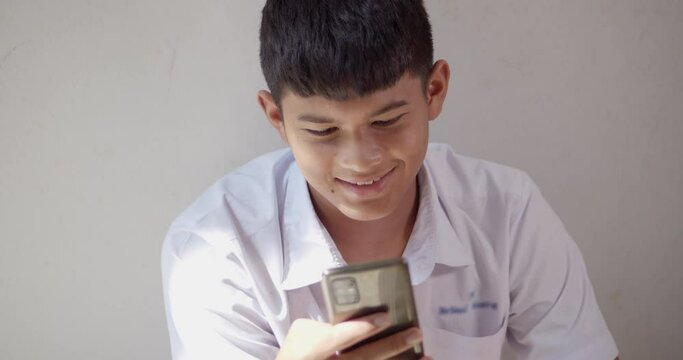 An Asian male high school student in a white school uniform is enjoying a happy smile on his smartphone on the Internet and social media.	