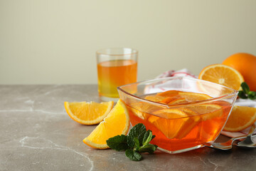 Concept of dessert with bowl of orange jelly with orange slices on gray table