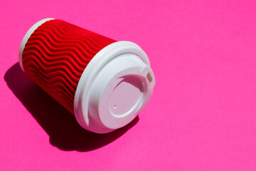 Red paper cup for coffee or tea to go on a pink background. Disposable tableware on a colored background with copy space.