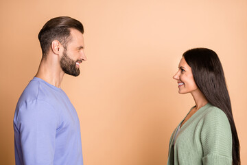 Profile side photo of young happy smiling cheerful couple husband wife look each other isolated on beige color background