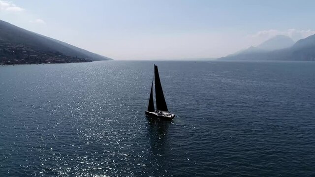 Aerial slow motion view of yacht moving over mountainous lake showing the quiet water and mountains left and right of the screen beautiful peaceful vacation scene shot during summer season 4k