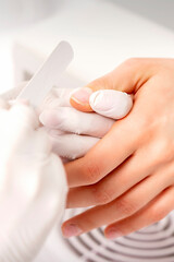 Manicure master wears white gloves with nail file doing manicure on female fingernails in a nail salon