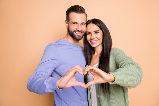 Photo of young happy smiling cheerful positive couple husband wife showing heart isolated on beige color background