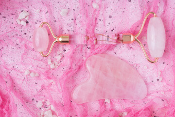 Pink Gua Sha facial massage tools. Rose Quartz jade roller on rose background