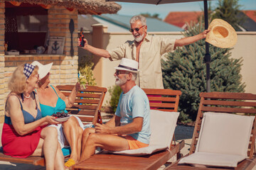 Obraz na płótnie Canvas Senior friends having fun by the pool, drinking cocktails
