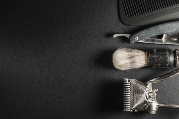 On a black surface are old barber tools.Two vintage manual hair clipper, comb, razor, shaving brush, hairdressing scissors. black monochrome. Close-up. Barbershop background. contrast shadows.