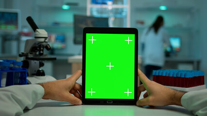 POV shot of chemist using tablet with green screen in biological laboratory. Medical worker wearing white coat in clinic working with notebook with chroma key on isolated display in medical lab