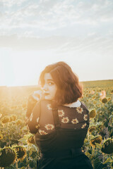 Fototapeta na wymiar A beautiful girl is looking at the camera with her sunflowers shirt in a field of sunflowers