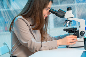 Fototapeta premium Young woman student working on a microscope while sitting at the table